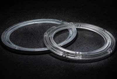 Zwei transparente, runde Ringe mit gezacktem Rand liegen übereinander. Sie sind aus glattem Material gefertigt und auf einem dunklen Untergrund positioniert, was einen Kontrast schafft.