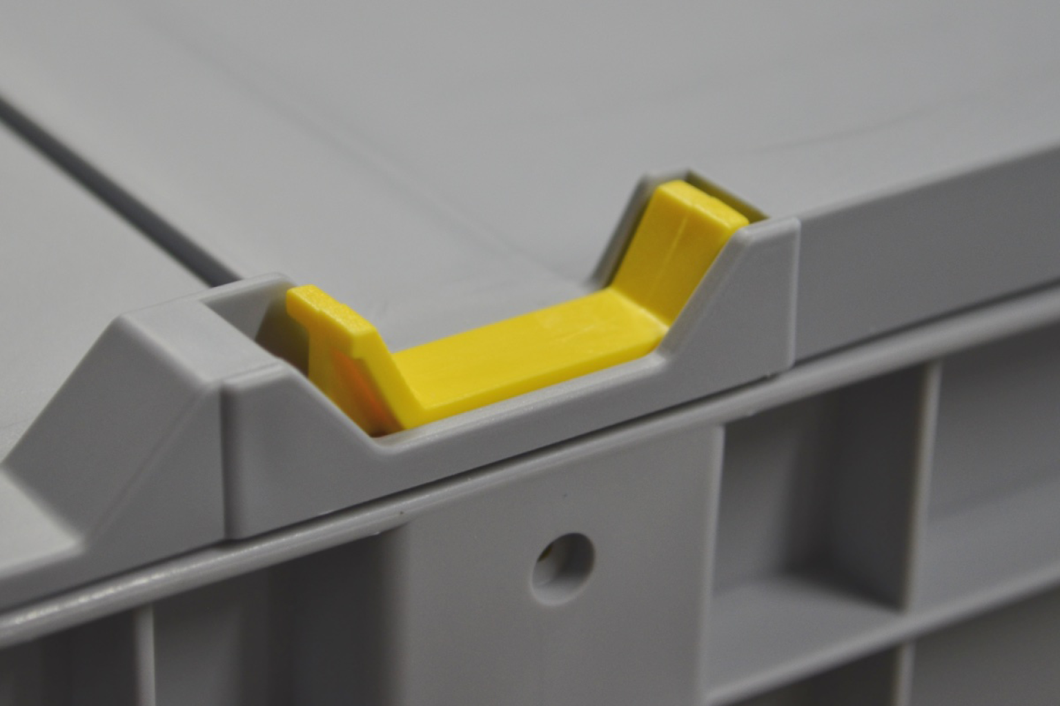 A gray storage box features a distinctive yellow latching mechanism on its edge, designed for secure closure. The background is neutral, emphasizing the box-s details and construction.