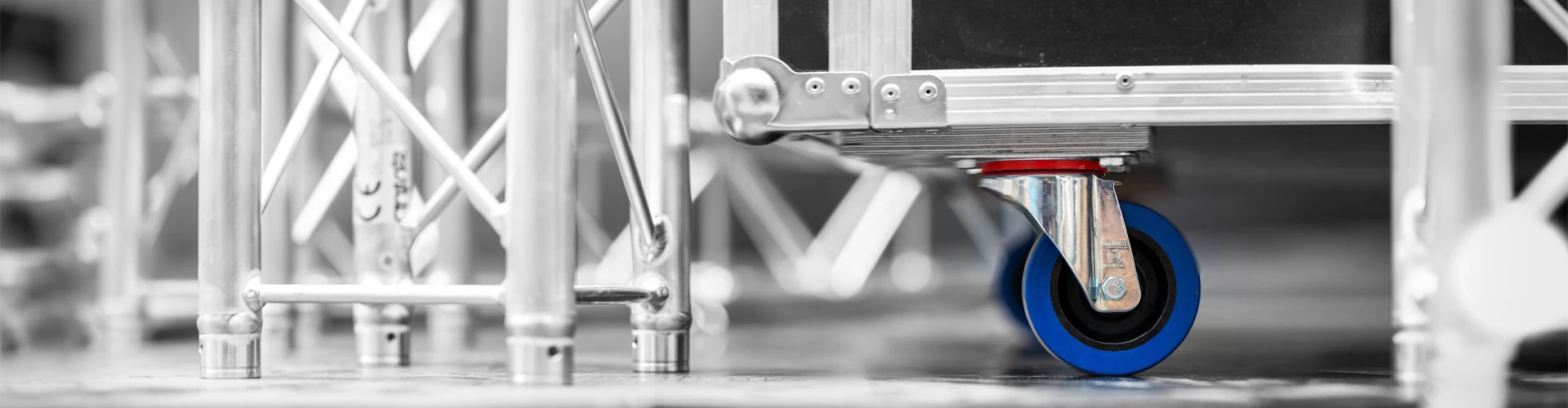 Industrielles Rad mit blauer Gummibereifung, montiert an einem Aluminiumgestell. Das Rad ist sichtbar in einem Betriebsumfeld, umgeben von weiteren Gestellen und einem glänzenden Boden.