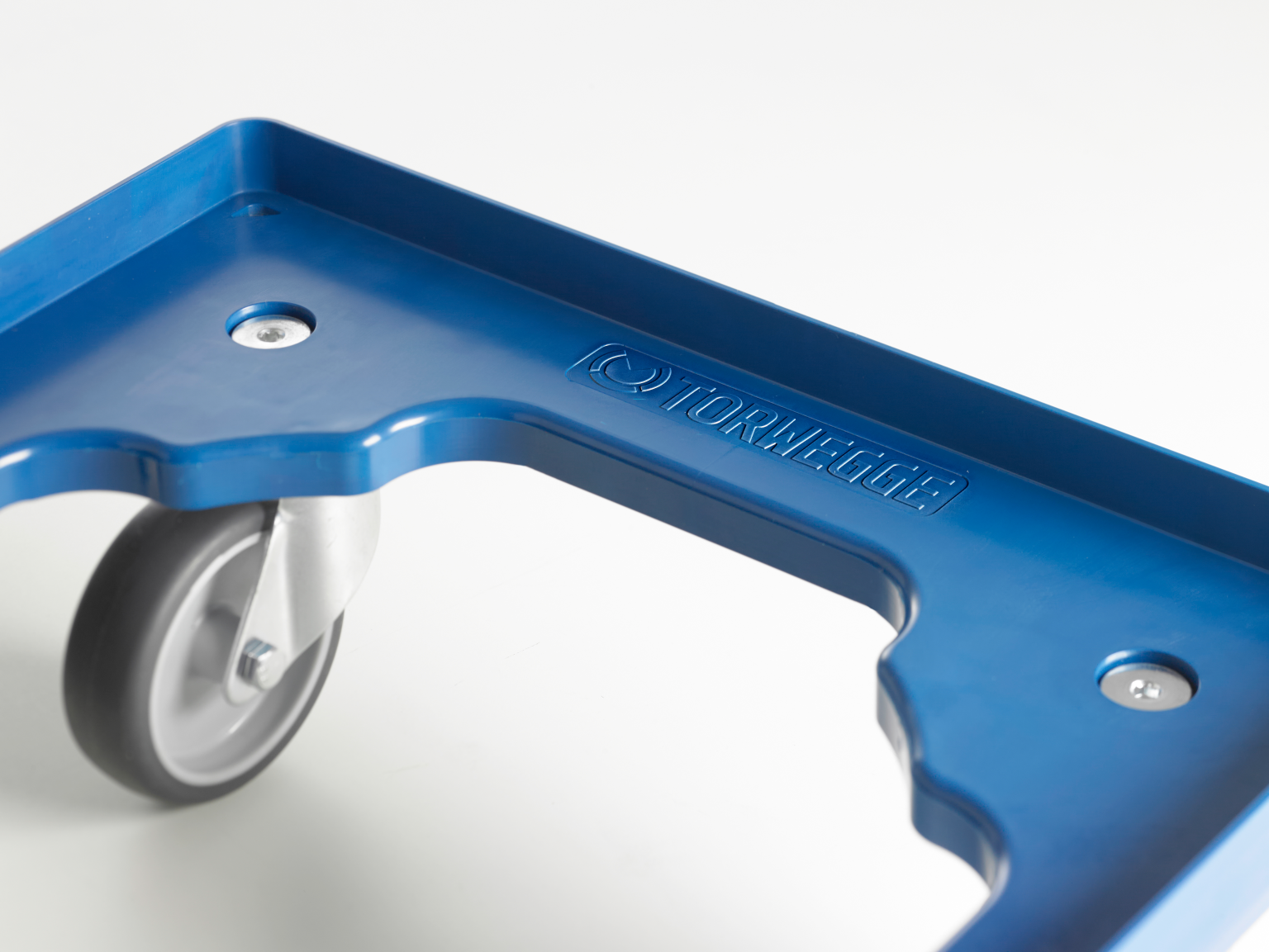 A blue transport trolley features a smooth plastic surface with rounded edges and a visible wheel in the corner. The logo -TORWEGGE- is embossed on the surface, indicating its brand.