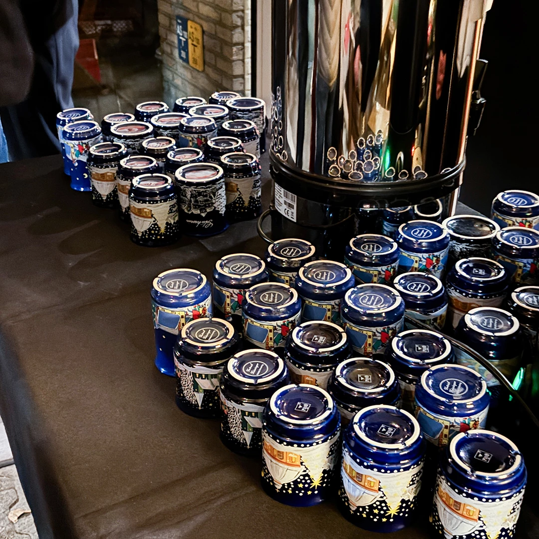 Blaue und bedruckte Gläser stehen auf einem Tisch, umgeben von einem glänzenden Kaffeeautomaten. Es gibt diverse festliche Motive auf den Gläsern, die ordentlich angeordnet sind.